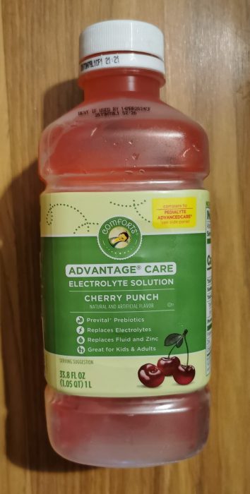A bottle of Comforts Advantage Care Cherry Punch Electrolyte Drink laying on a hardwood floor